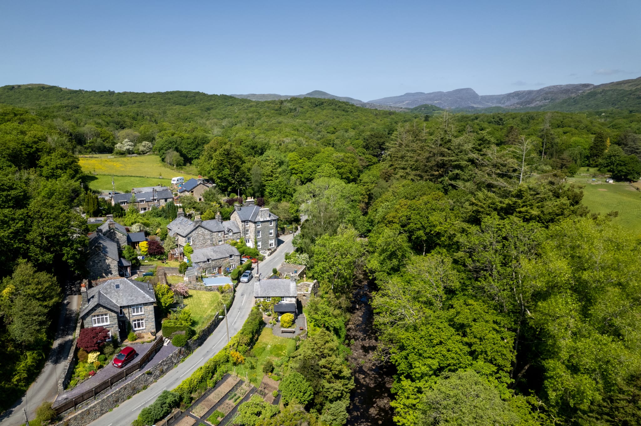 Gwynfryn House and the village of Llanbedr from above, set in the wooded Artro valley with the mountains of Snowdonia beyond